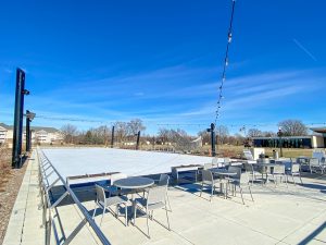 The sky is blue and the ice rink is white. Chairs surround the one side of the ice rink.