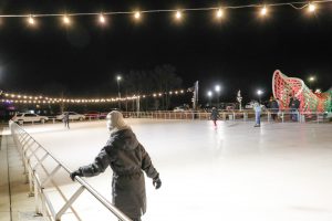 Kids skating on the ice rink and it's dark, but lights illuminate the rink.